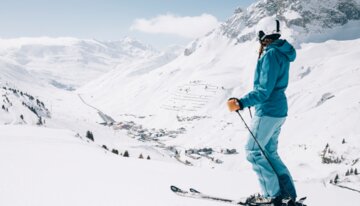 © Daniel Zangerl, Lech Zürs Tourismus Una sciatrice con abbigliamento da sci blu è ferma sulla pista e guarda in lontananza. | © Daniel Zangerl, Lech Zürs Tourismus