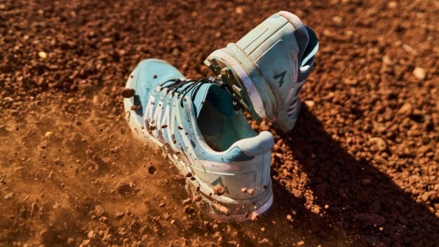 Two blue sports shoes on a brown surface with dust kicking up.