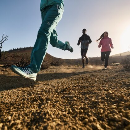 Three people running on a dusty trail.