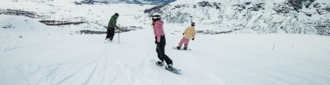 Zwei Snowboarder und ein Skifahrer fahren einen schneebedeckten Berg hinab.