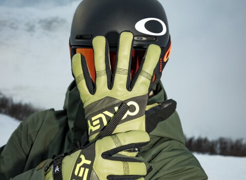 Mann im grünen Skianzug mit passender Oakley Skibrille und Oakley  Skihandschuhen hält die linke Hand offen vor das Gesicht während die rechte Hand das linke Handgelenk umgreift.  | © 30.09.2026
