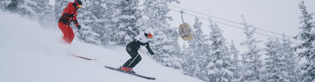 Due sciatori scendono una pista innevata sotto un impianto di risalita. | © INTERSPORT International Corporation GmbH