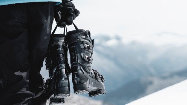 Ein Paar Skischuhe werden von einer Person vor einer verschneiten Bergkulisse gehalten. | © Atomic Austria GmbH