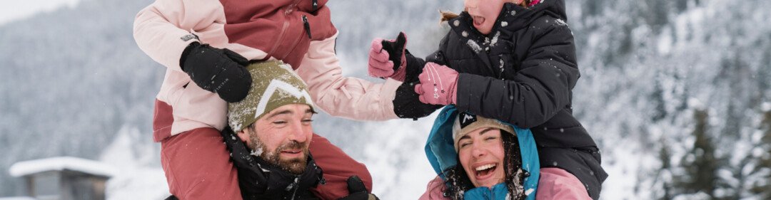 © INTERSPORT International Corporation GmbH Una famiglia si diverte sulla neve con i genitori che portano i figli a cavalluccio. | © INTERSPORT International Corporation GmbH