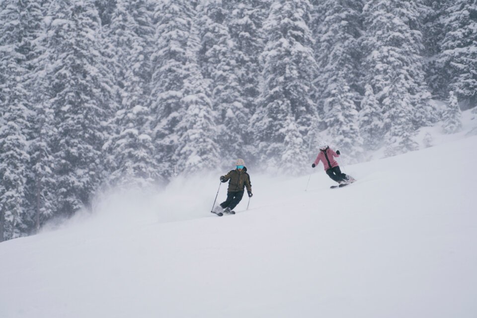 © INTERSPORT International Corporation GmbH Zwei Skifahrer auf einer schneebedeckten Piste vor bewaldetem Hintergrund. | © INTERSPORT International Corporation GmbH