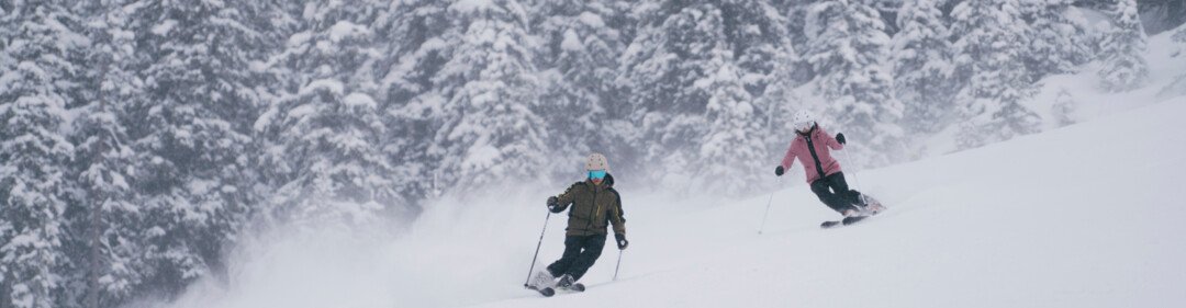 Due sciatori su una pista innevata con uno sfondo boschivo. | © INTERSPORT International Corporation GmbH