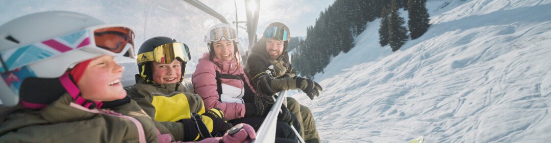 © INTERSPORT International Corporation GmbH Famiglia che viaggia su una seggiovia in una giornata di sole. | © INTERSPORT International Corporation GmbH