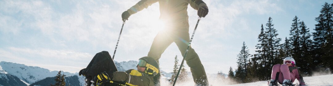 © INTERSPORT International Corporation GmbH Sciatore che cade e viene sorvolato con gli sci, con un bambino seduto sullo sfondo. | © INTERSPORT International Corporation GmbH