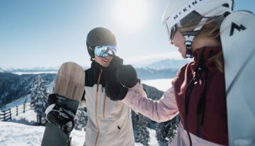 © INTERSPORT International Corporation GmbH Zwei Snowboarder geben sich die Hand im Schnee. | © INTERSPORT International Corporation GmbH