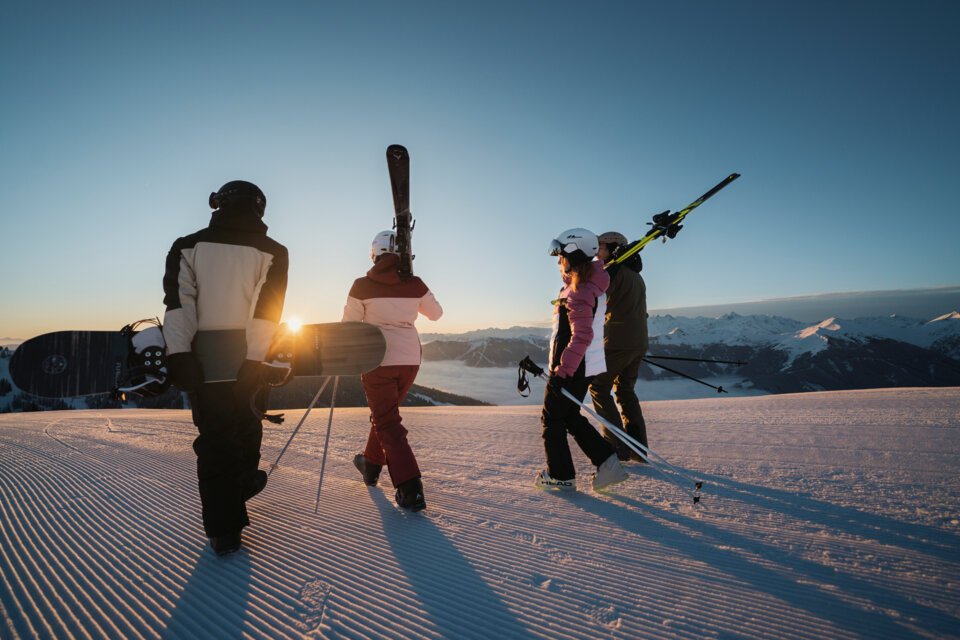 Group of skiers and snowboarders walking at sunset on a groomed slope. | © INTERSPORT International Corporation GmbH