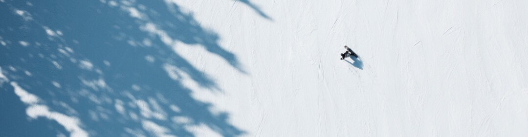 Vista aerea di sciatori e snowboarder su una pista innevata con ombre di alberi. | © INTERSPORT International Corporation GmbH