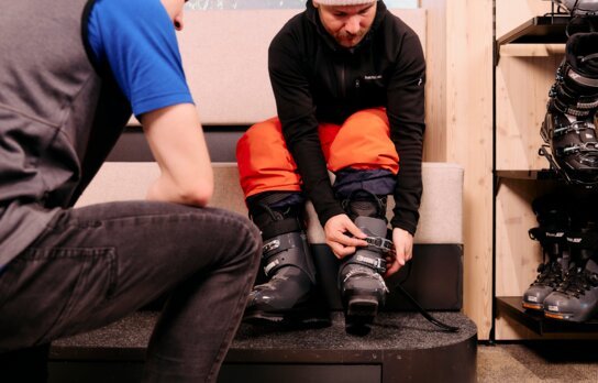 Mann schließt Skischuh mit Hilfe eines Verkäufers.