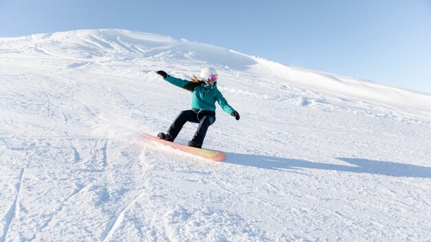 Snowboarderin fährt einen schneebedeckten Hang hinunter. | © Rossignol