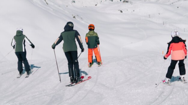 Vier Personen fahren Ski auf einer Skipiste.