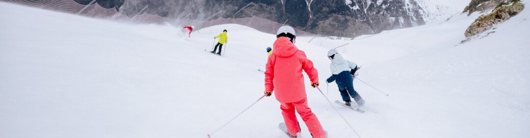 Skifahrer auf einer schneebedeckten Piste vor Bergkulisse.