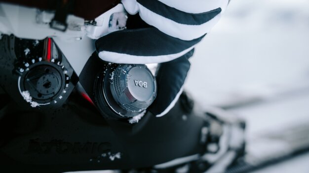 Detailaufnahme eines Skischuhs mit BOA-Verschluss und einer Hand im gestreiften Handschuh