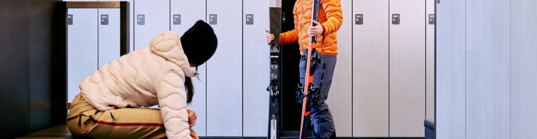 © ARMIN WALCHER Due persone si preparano per sciare in un deposito sci. | © ARMIN WALCHER