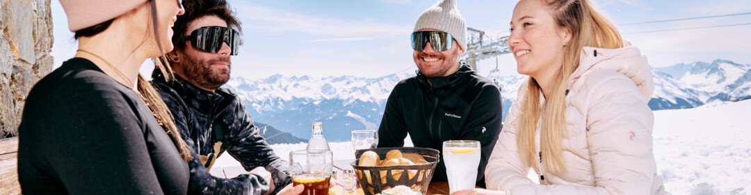 © ARMIN WALCHER Gruppo di amici che mangiano in un rifugio sciistico. | © ARMIN WALCHER