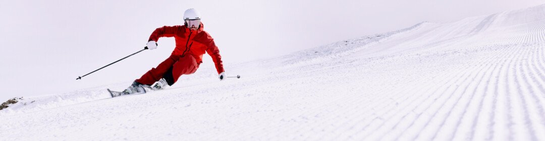 Scaitore in abito rosso su una pista innevata. | © ARMIN WALCHER