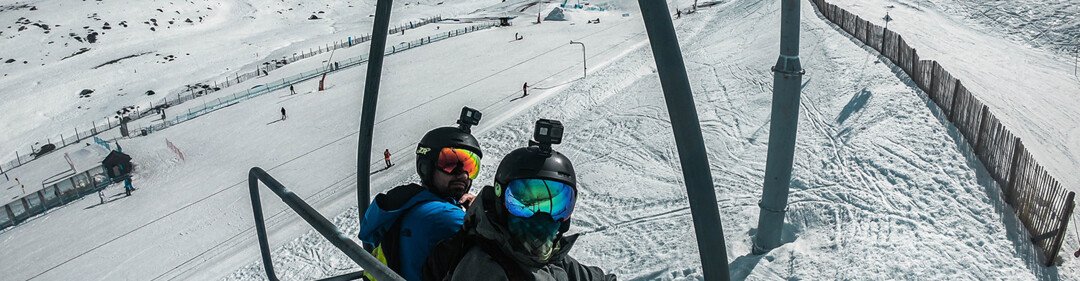 Due sciatori su una seggiovia con paesaggio montano innevato sullo sfondo.